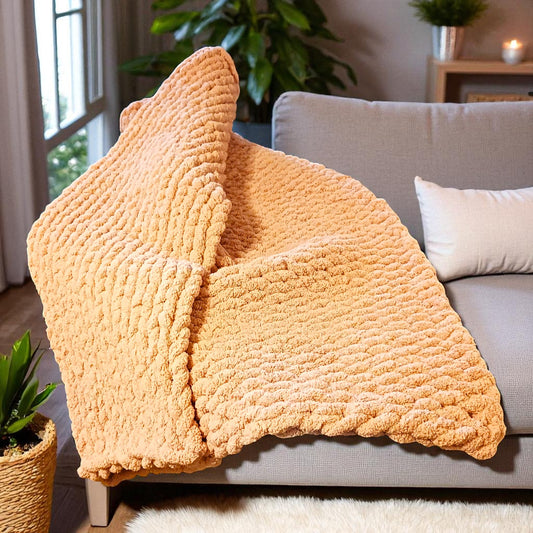 Blush chunky knit blanket draped over a gray sofa in a living room setting.