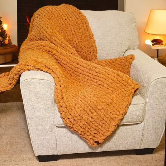 A chunky knit honeycomb pattern blanket in a butterscotch color draped over a chair.