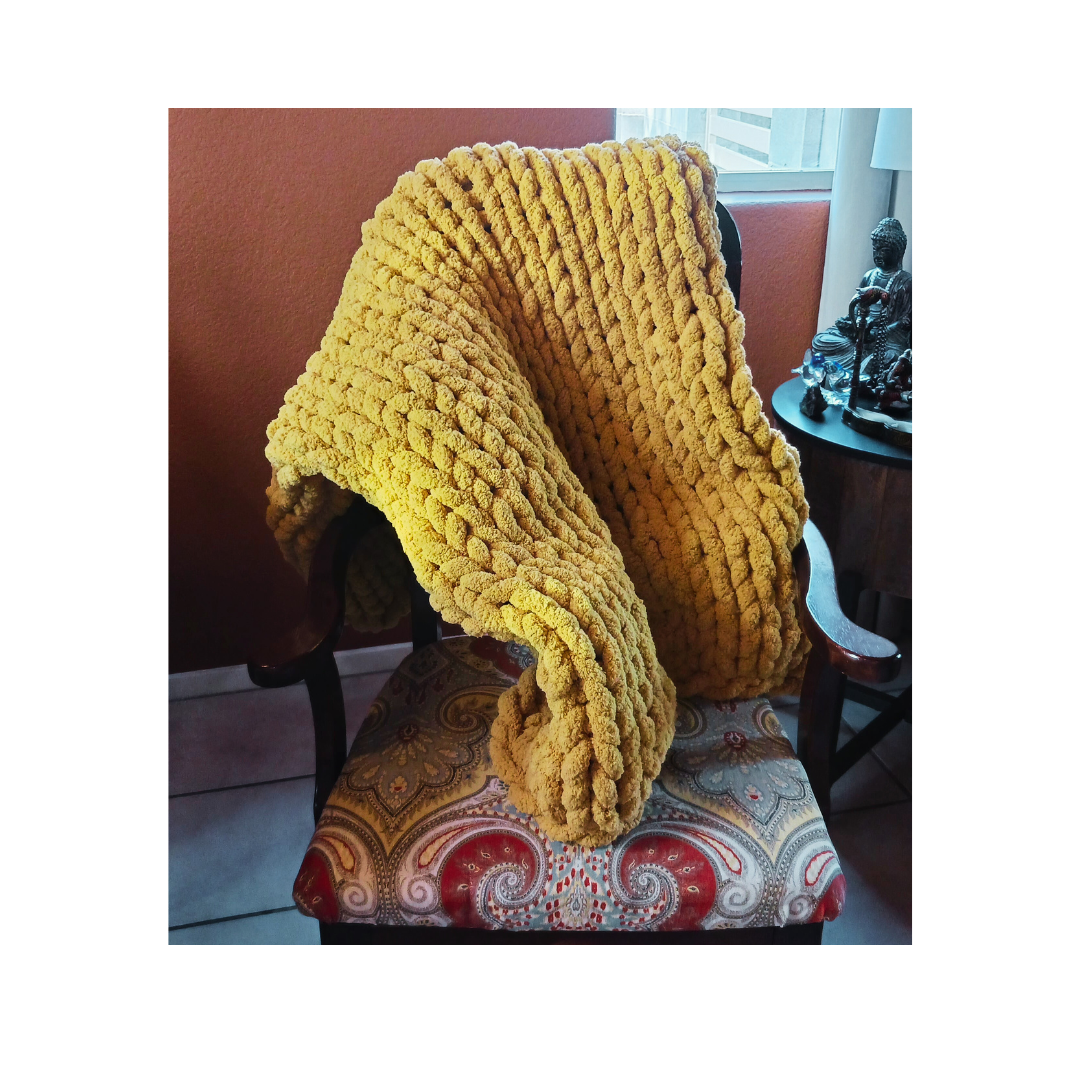 A thick, yellow, chunky knit blanket draped over a vintage wooden chair with an ornate cushion.