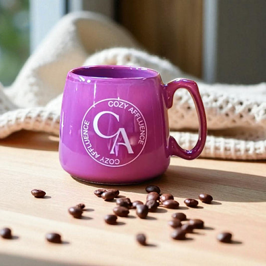 Purple mug with 'Cozy Affluence' logo on a wooden surface with scattered coffee beans.