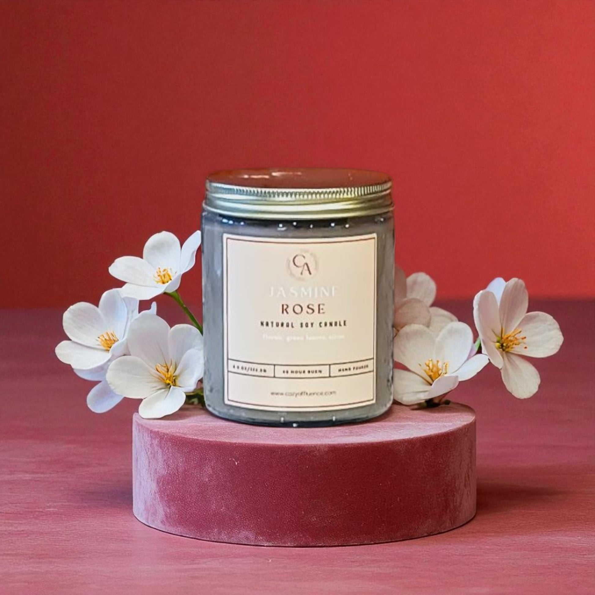 Candle labeled 'Jasmine Rose' with white flowers on a red background.