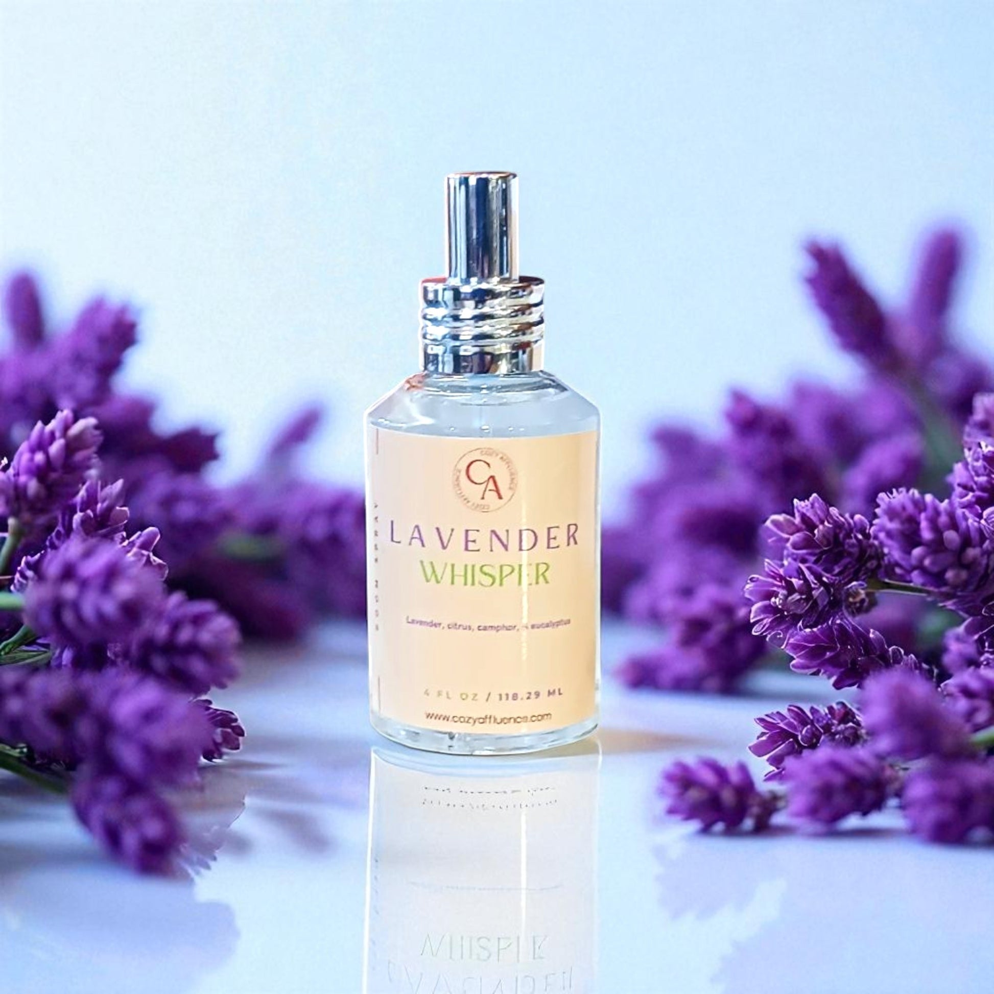Lavender room spray product with a bottle labeled 'Lavender Whisper' surrounded by lavender flowers on a light blue background.