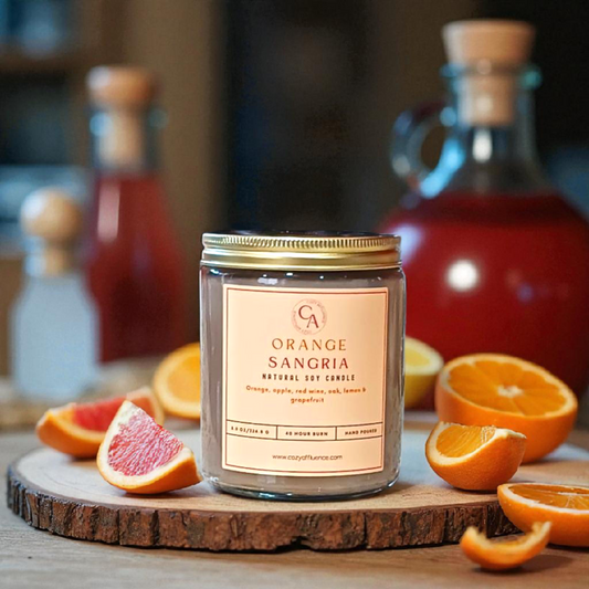 Candle labeled 'Orange Sangria' surrounded by oranges and bottles on a wooden surface