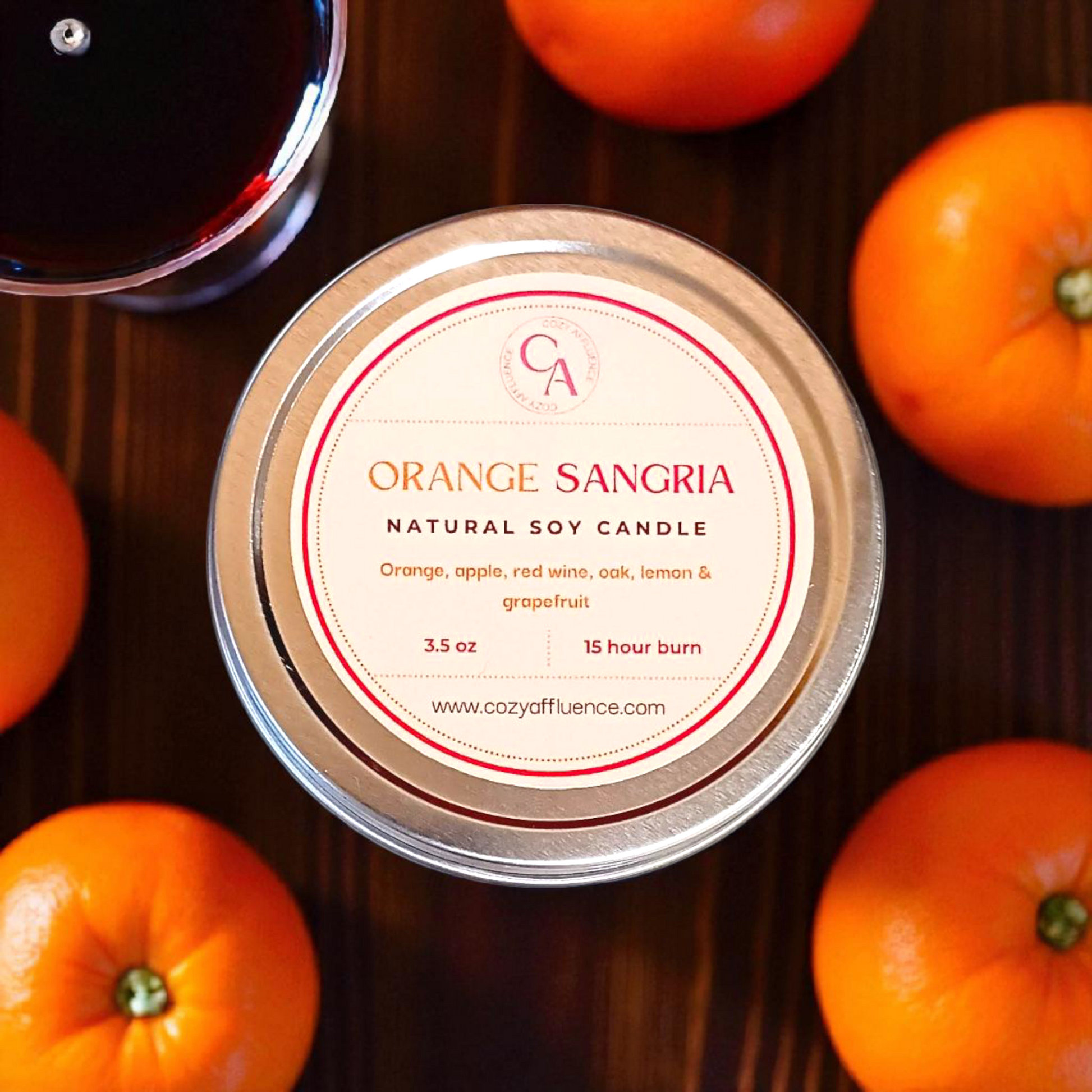 Orange Sangria candle with oranges and a glass of red wine on a wooden surface