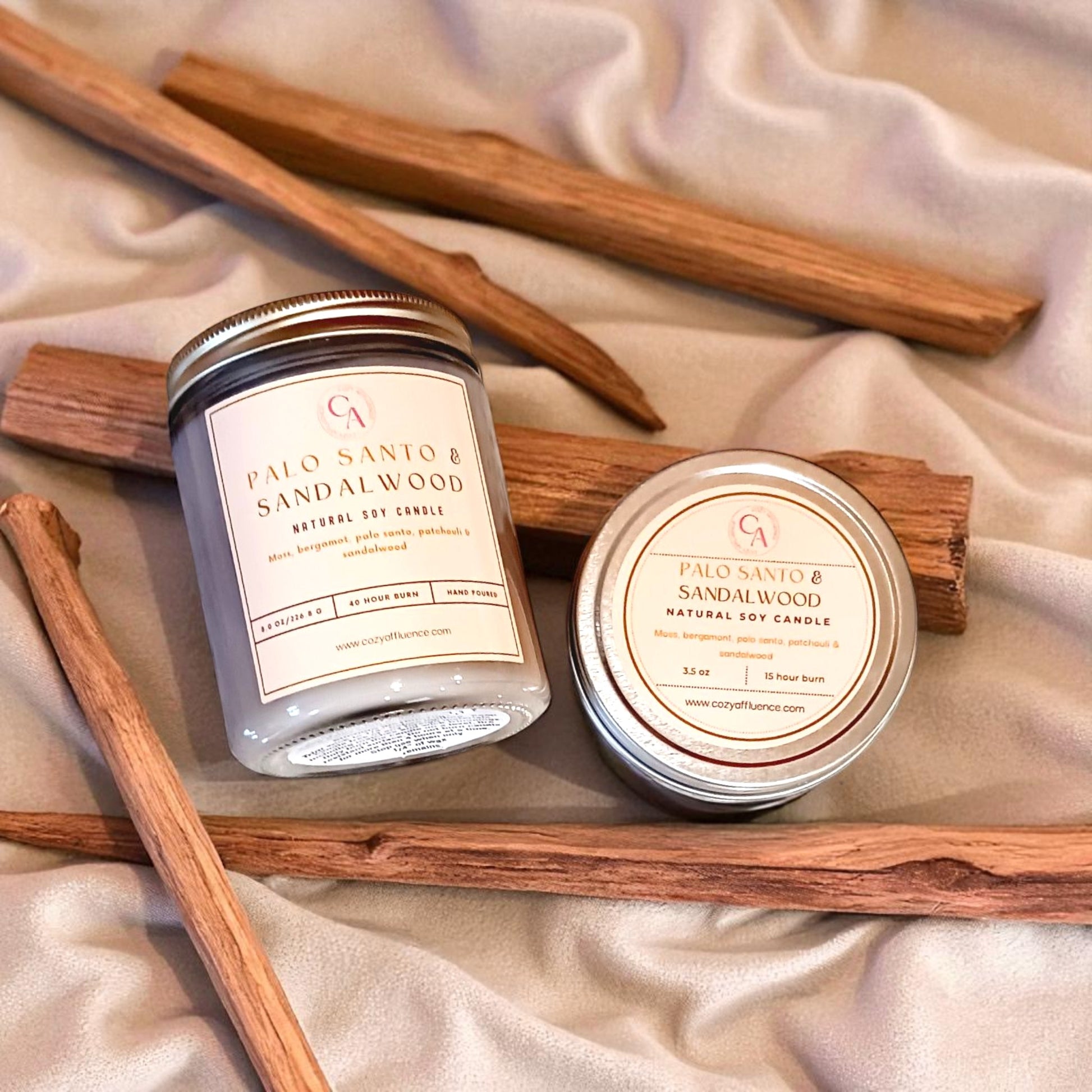 Two Palo Santo & Sandalwood candles 8oz and 3.5oz with cinnamon sticks on a beige fabric background.