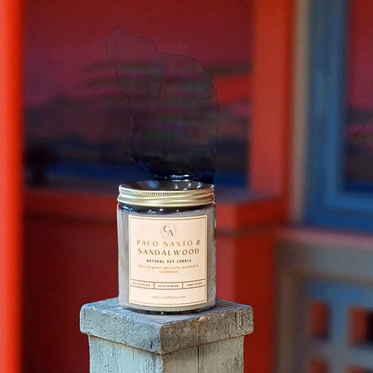 Candle labeled ' Palo Santo & Sandalwood' on a wooden block with a colorful background.