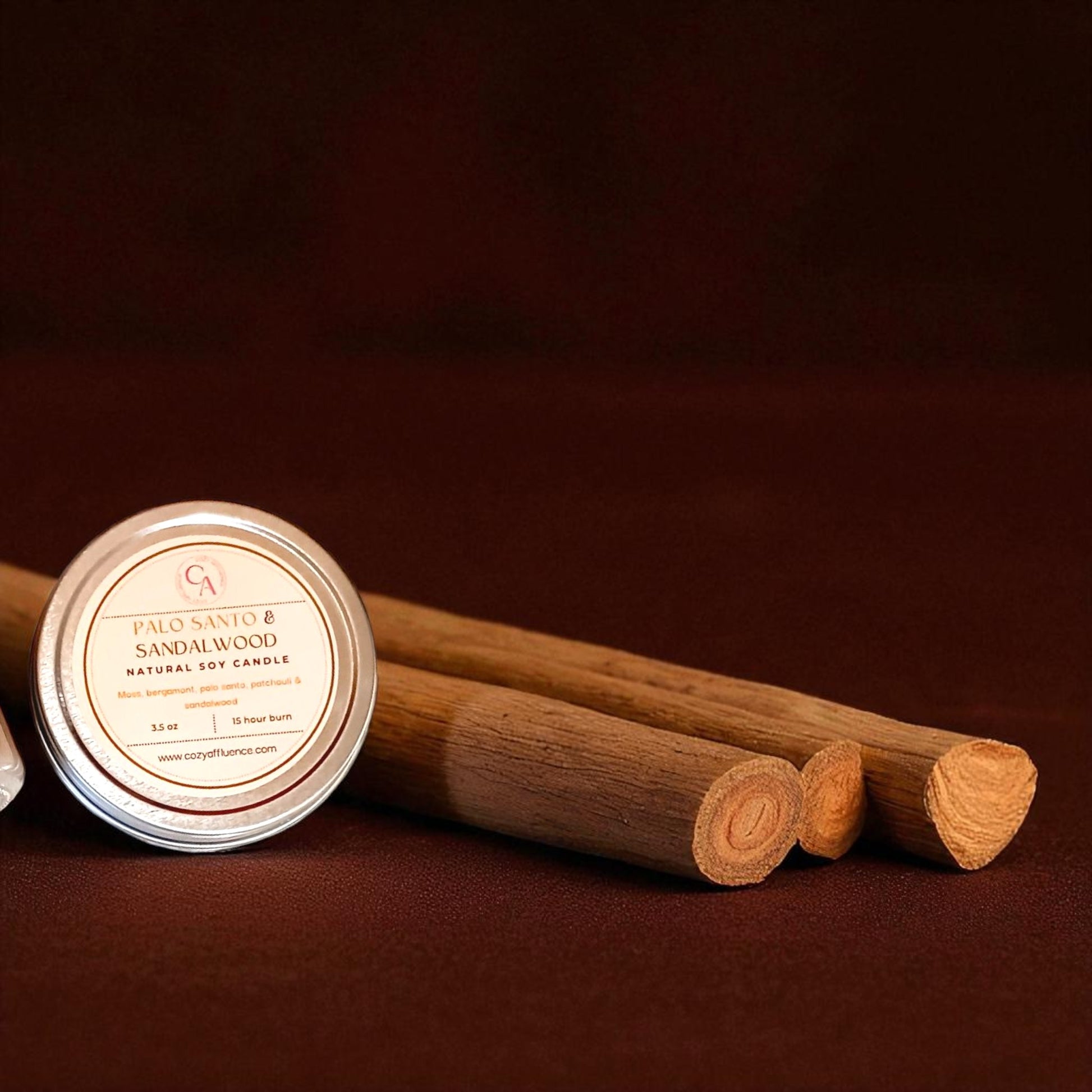 Natural soy candle labeled 'Palo Santo & Sandalwood' with three wooden sticks on a dark brown background.