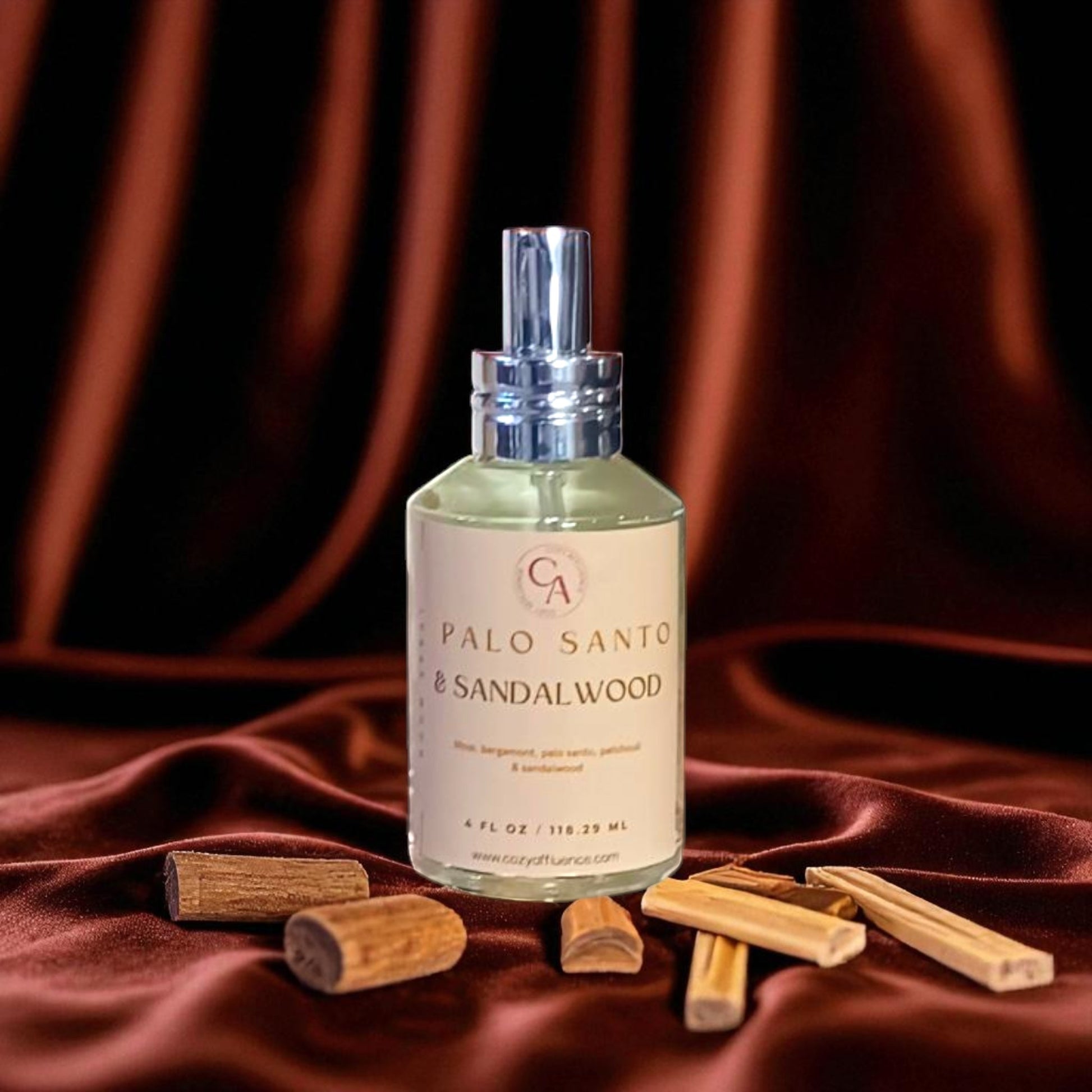 Bottle of Palo Santo & Sandalwood room spray with wooden sticks on a red fabric background.