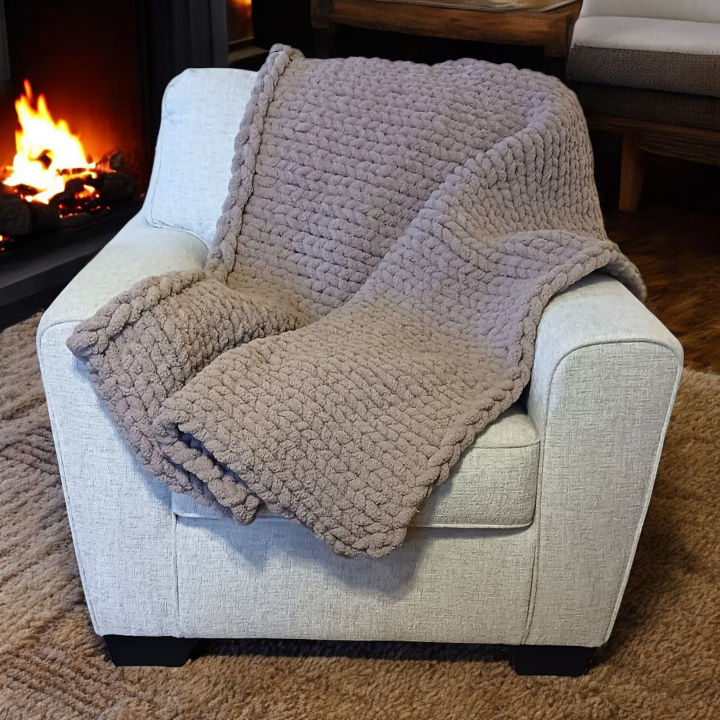 A beige chunky knit blanket draped over a chair with a fireplace in the background.