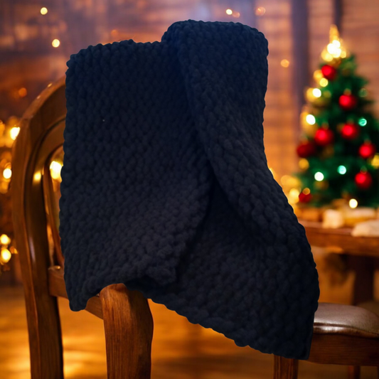 A black chunky knit blanket draped over a chair with a festive Christmas tree in the background.