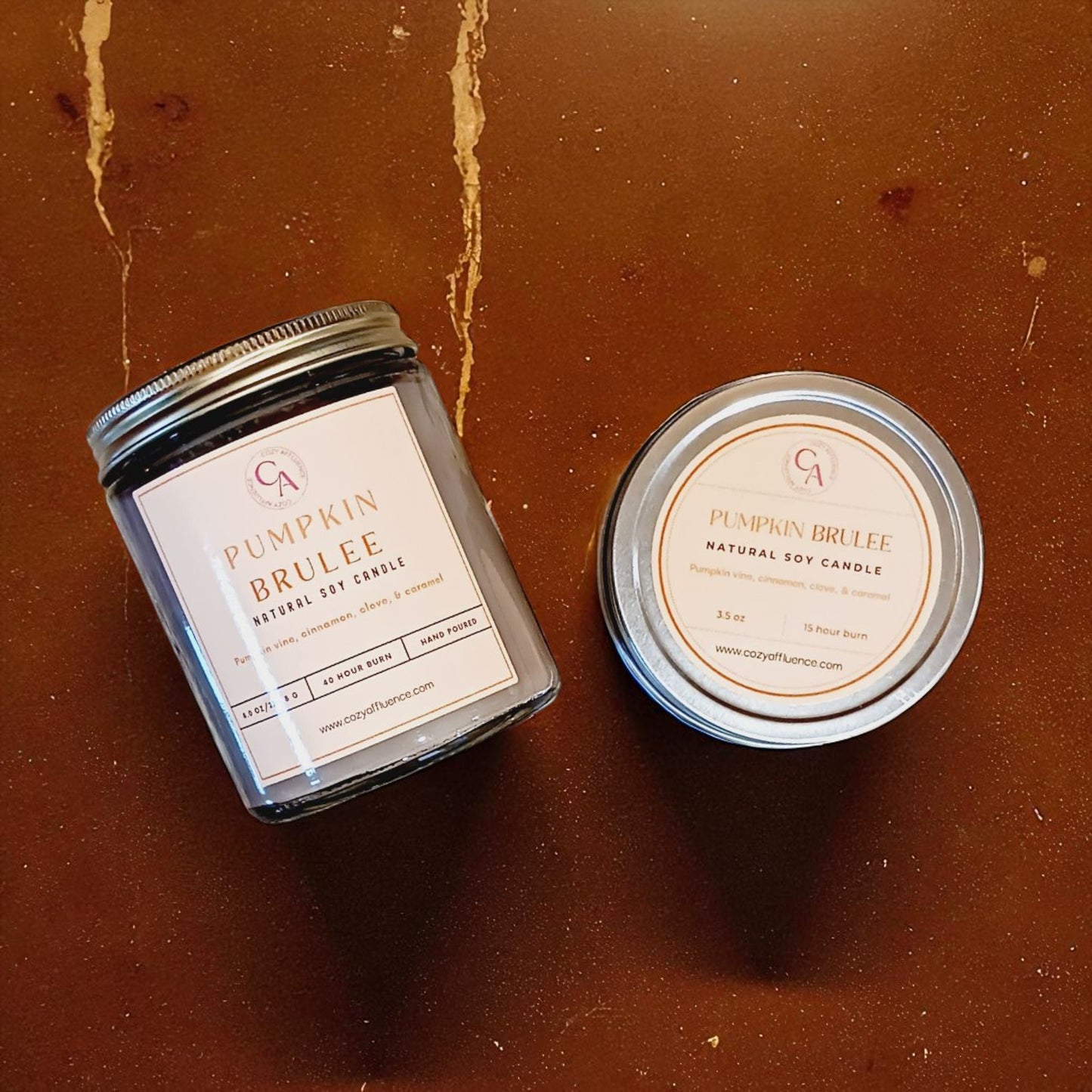 Two candles labeled 'Pumpkin Brulee' on a brown surface.