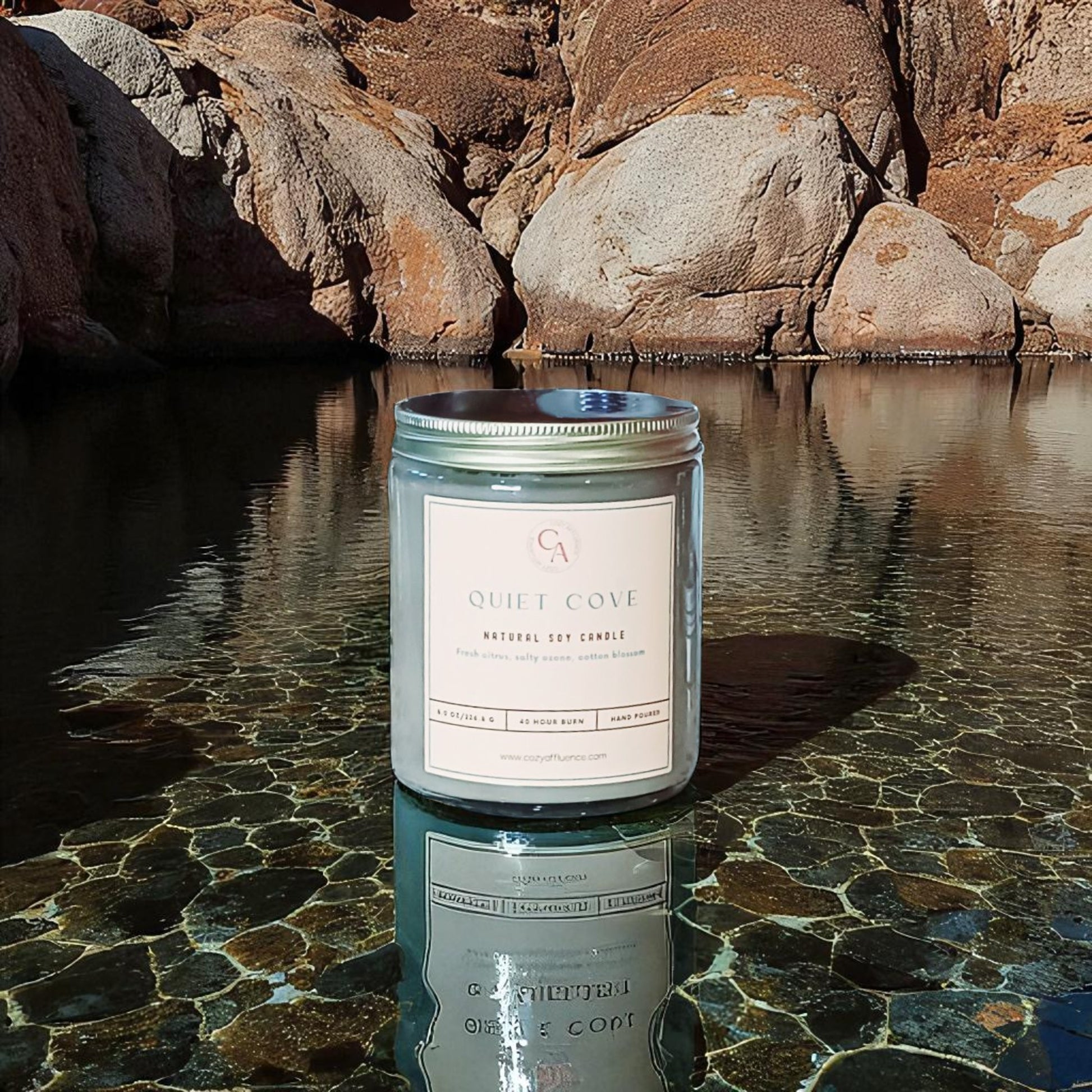Candle labeled 'Quiet Cove' on a reflective water surface with rocks in the background