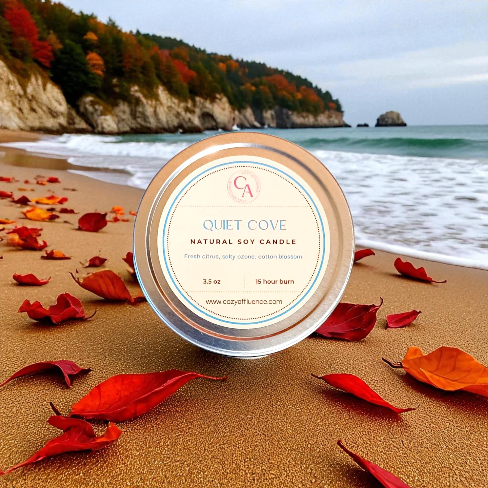 Natural soy 3.5 oz candle with 15 hour burn time labeled 'Quiet Cove' on a beach with autumn leaves and ocean view.