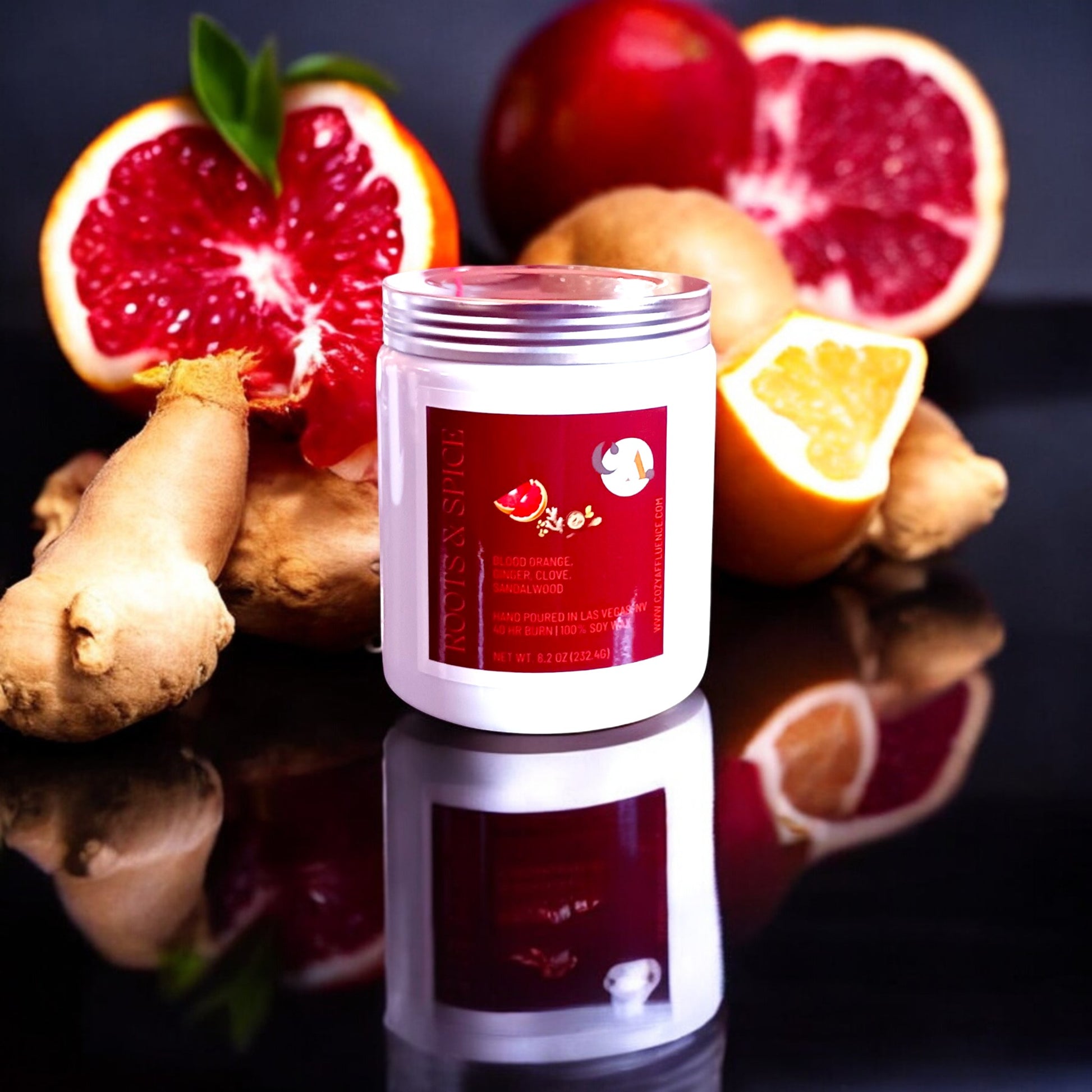 A white jar candle labeled "Roots & Spice" with notes of blood orange, ginger, clove, and sandalwood, displayed alongside fresh ginger roots and sliced blood oranges.