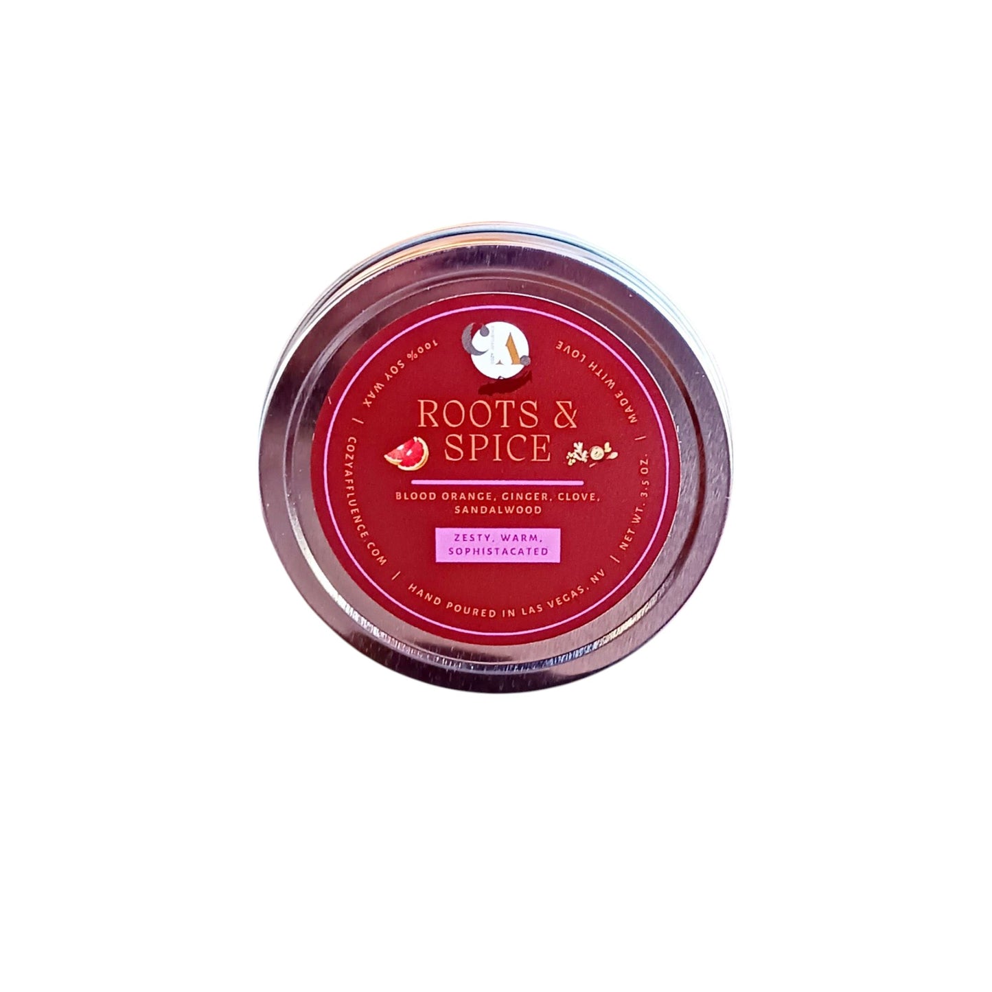 A round tin candle labeled "Roots & Spice" with notes of blood orange, ginger, clove, and sandalwood, described as zesty, warm, and sophisticated, hand poured in Las Vegas, NV.