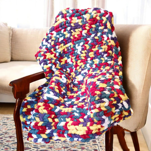 Folded watercolor chunky knit blanket thrown over a chair in a living room scene.