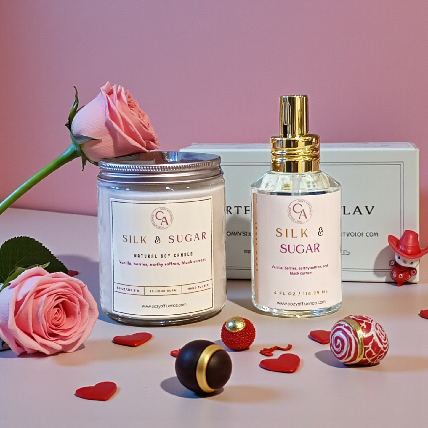 Silk & Sugar candle and perfume bottle with pink roses and decorative items on a light surface.