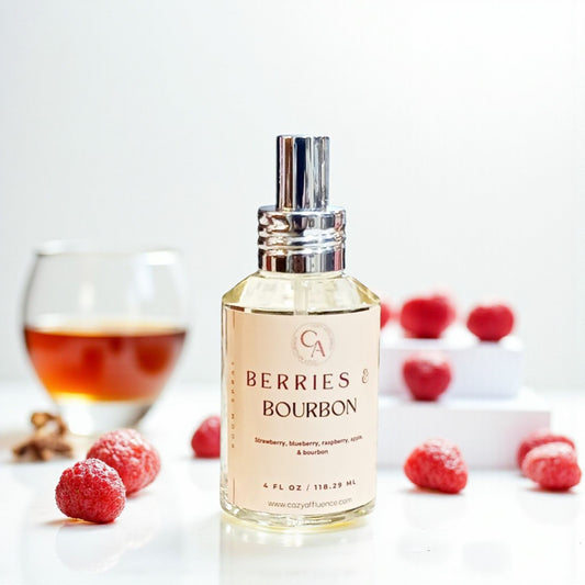 Bottle of 'Berries & Bourbon' room spray with raspberries and a glass of bourbon in the background.