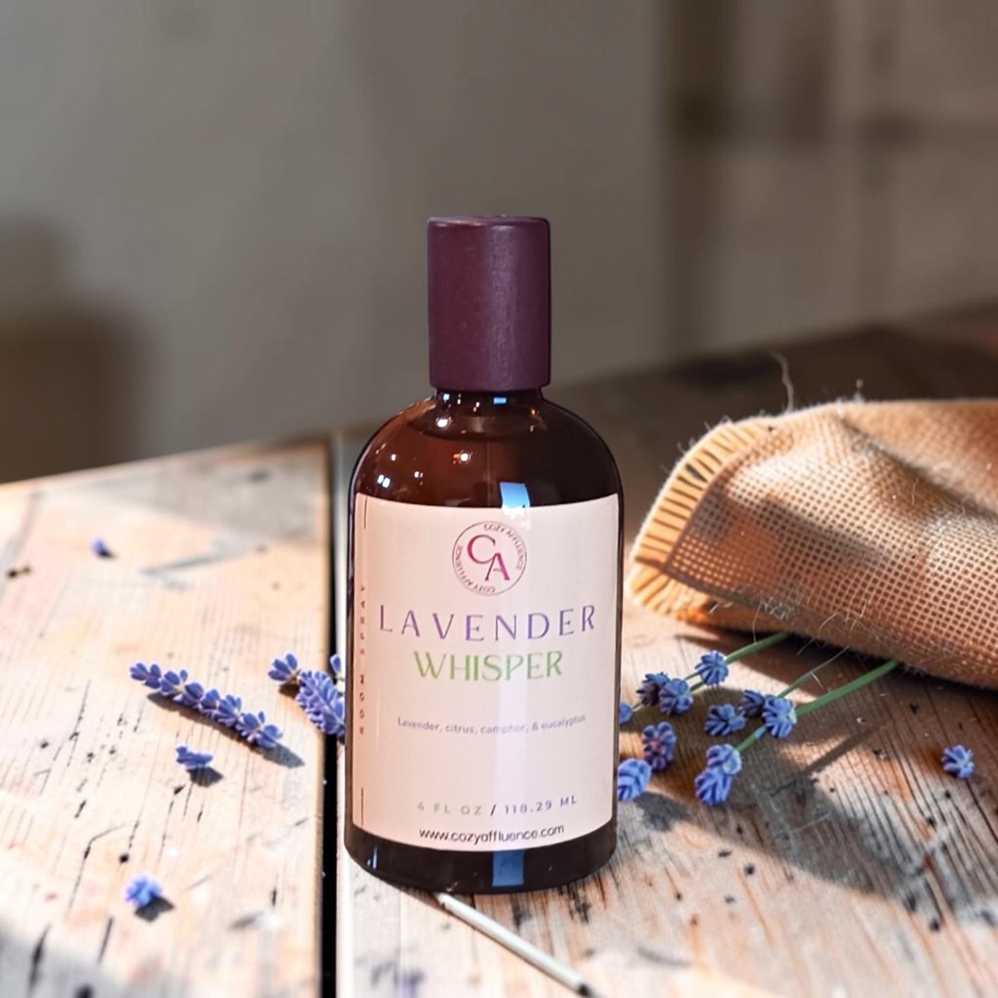 Bottle of 'Lavender Whisper' on a wooden surface with lavender flowers.
