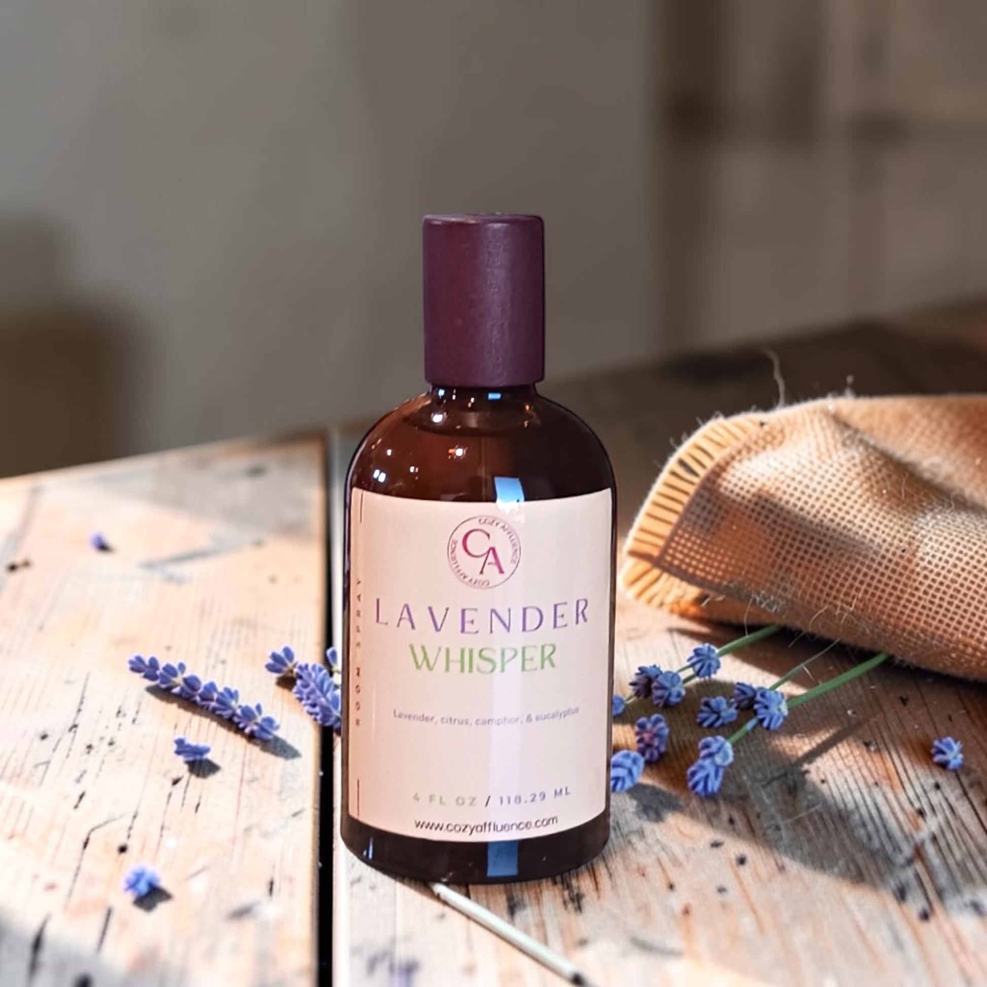 Bottle of 'Lavender Whisper' on a wooden surface with lavender flowers.