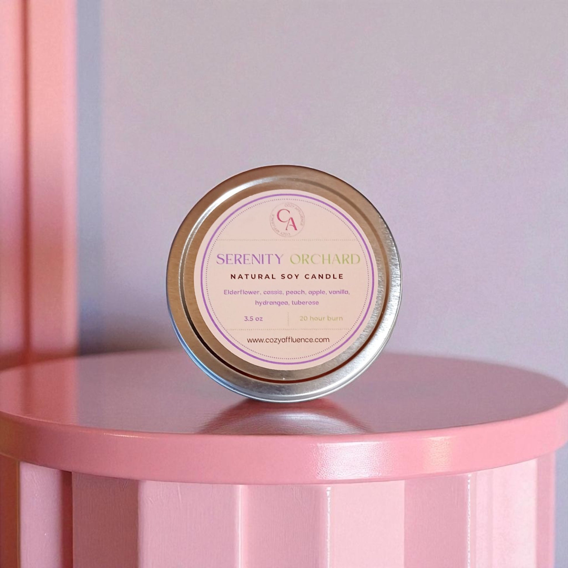 Scented natural soy candle tin labeled 'Serenity Orchid' on a pink surface with a soft pastel background.