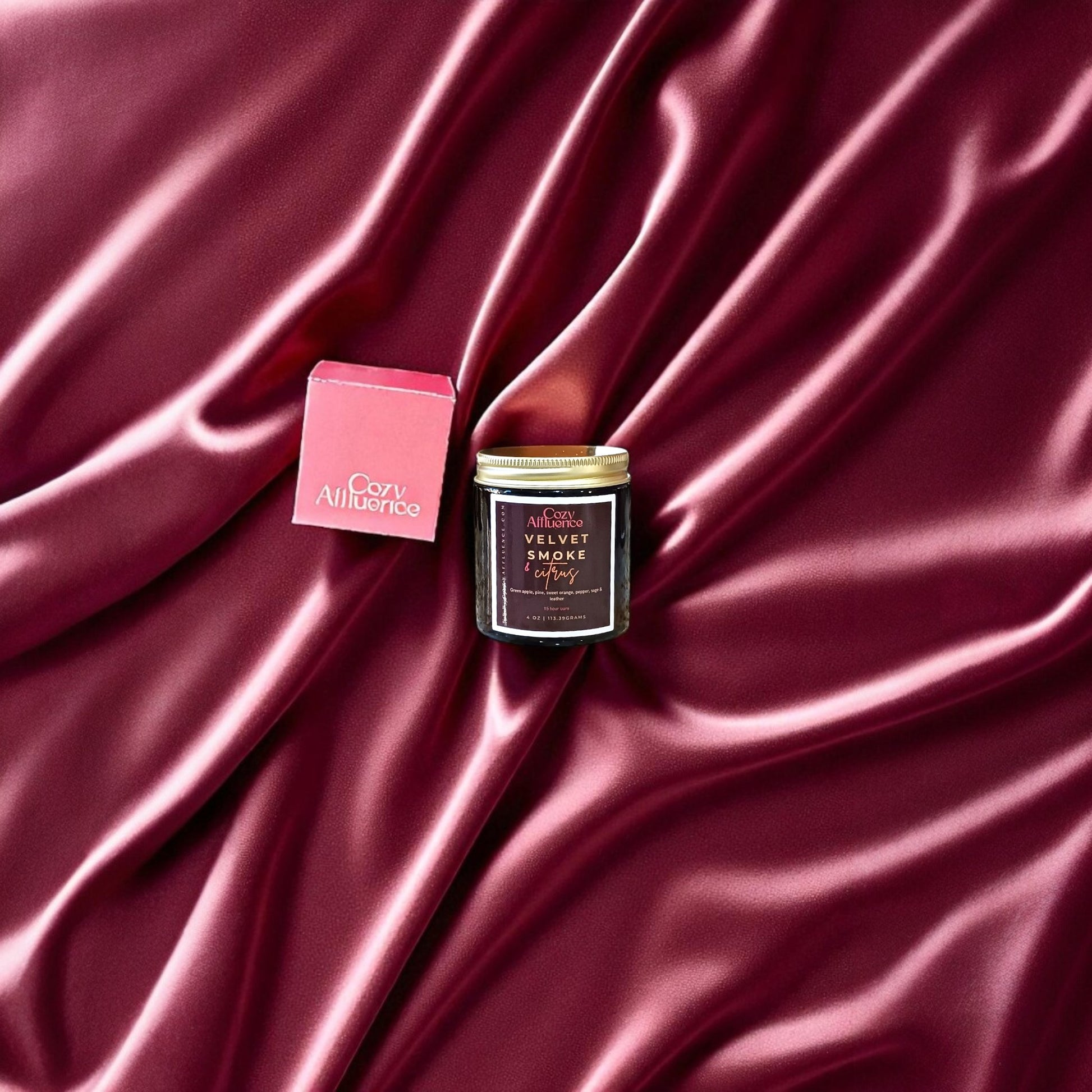 Velvet Smoke & Citrus Candle with it's box on a burgundy satin background.