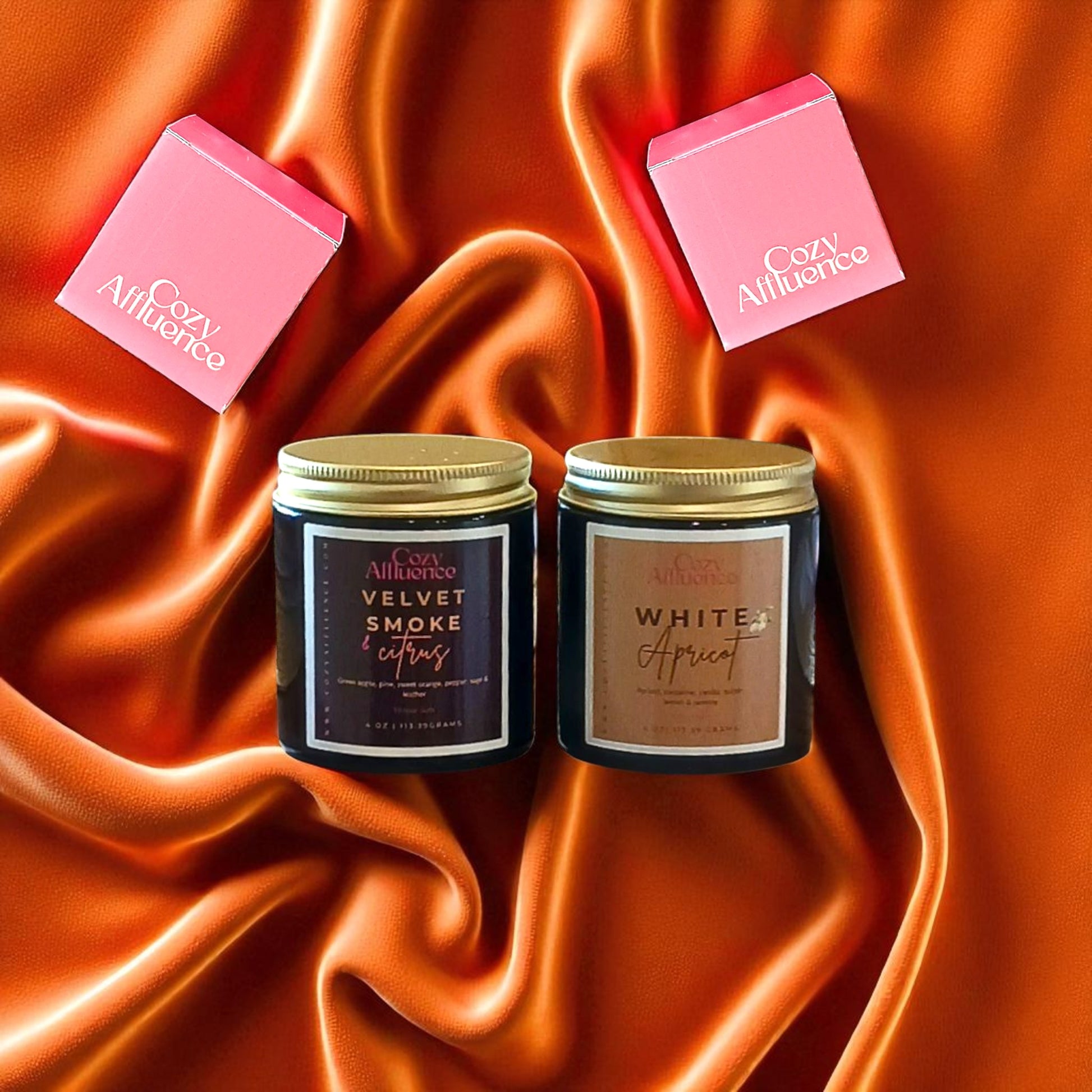 Two candles with labels on a satin background, with 'Cozy Affluence' boxes.