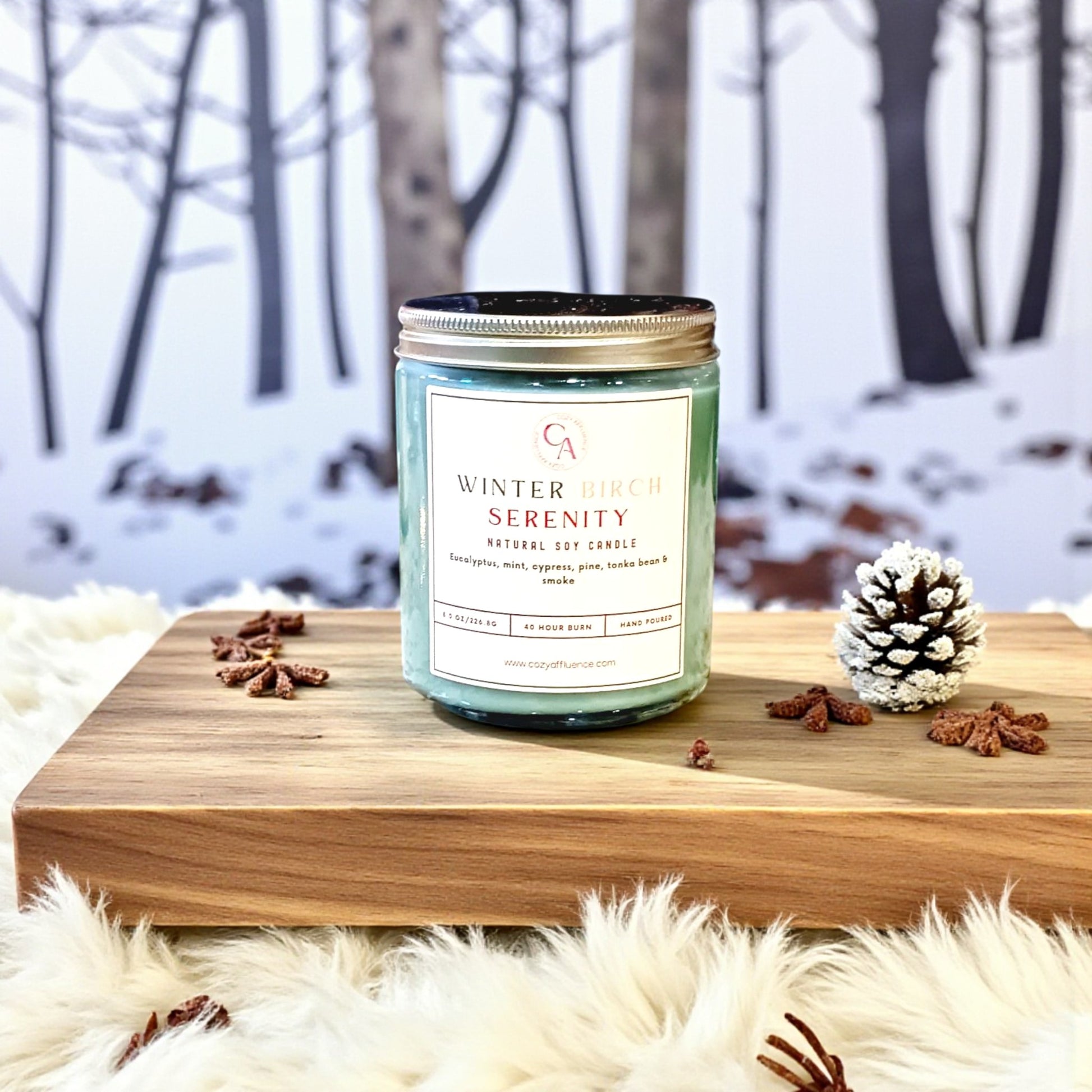 Candle labeled 'Winter Serenity' on a wooden surface with a snowy forest background