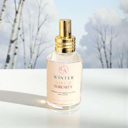 Bottle of 'Winter Birch Serenity' perfume with a gold spray top against a snowy background.